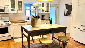 A modern kitchen with white cabinetry, a central island with stools, a large pendant light, and a view to the outside.