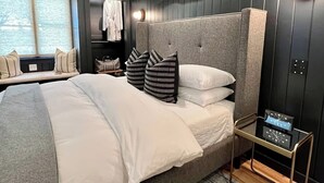 A modern hotel room with a large bed, a bedside table with a clock, and a window with blinds.