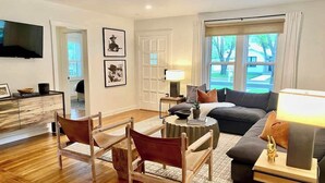 A modern living room with a wooden floor, a sofa, a coffee table, and a TV mounted on the wall.