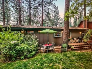A patio with a table and chairs, surrounded by greenery and trees. - LAKE TAHOE HAVEN VACATION HOME (South Lake Tahoe)
