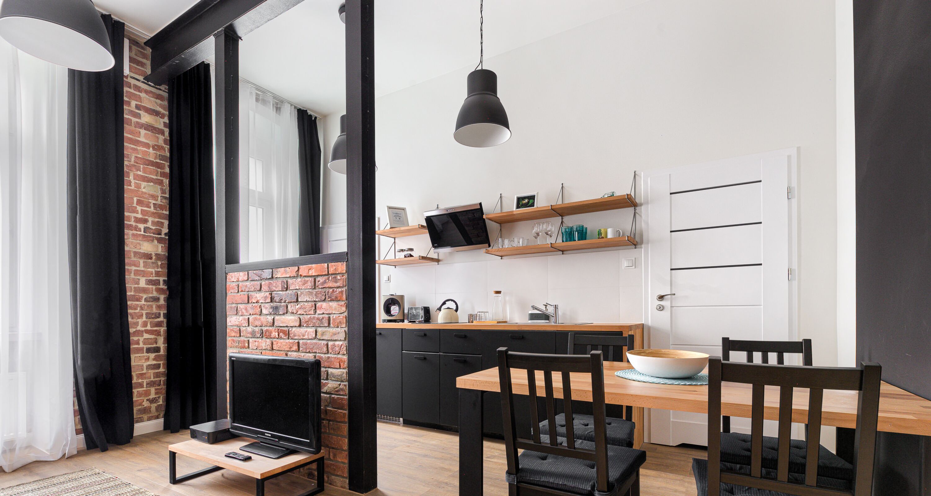 A modern kitchen with a brick wall, wooden cabinets, and a dining area with a wooden table and chairs.