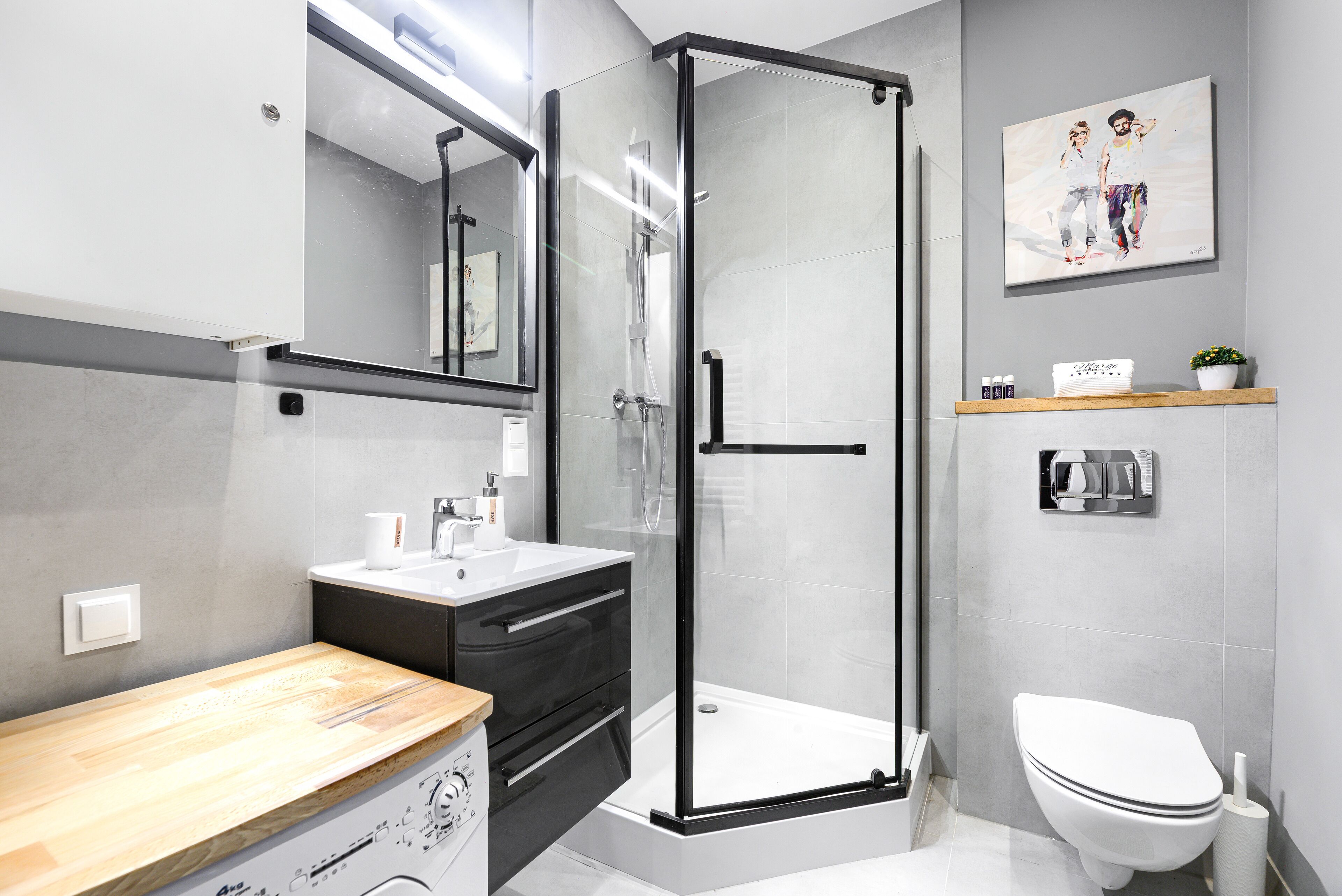 Un baño moderno con cabina de ducha de vidrio, inodoro blanco, tocador de madera y estante con artículos de aseo.