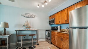 Una cucina con mobili in legno, elettrodomestici in acciaio inossidabile, uno sgabello da bar e un cartello con la scritta 'Welcome to the Beach'.