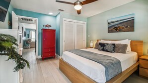 Camera da letto con un letto, una ventola a soffitto, un armadio rosso e un quadro a tema spiaggia.