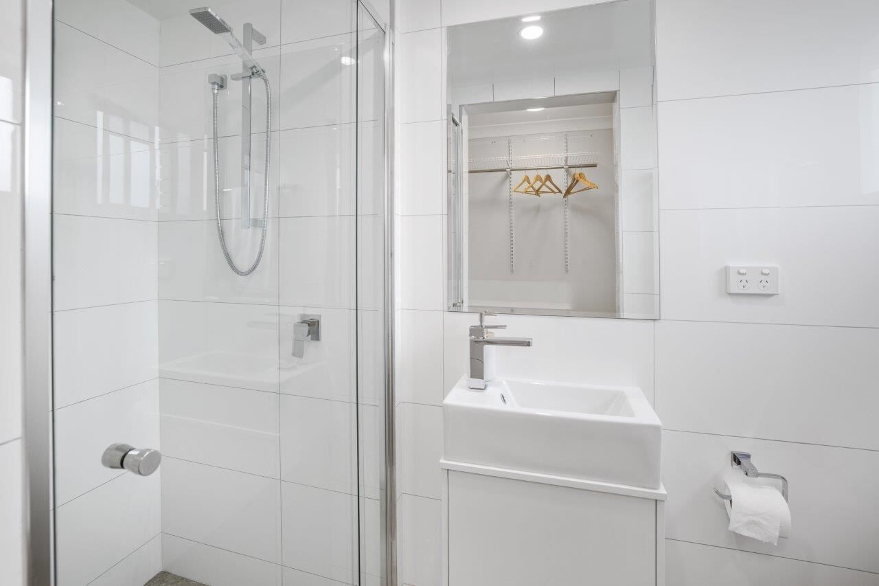 Une salle de bain moderne avec une douche à parois de verre, un lavabo blanc et un miroir au-dessus.