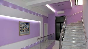 A modern interior with a purple wall, a glass railing, and a marble staircase. - White City (Berat)