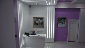 A reception area with a modern design, featuring a reception desk, a framed cityscape painting, and a door. - White City (Berat)