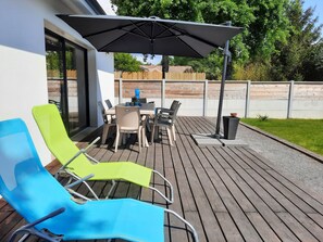Een terras buiten met een tafel, stoelen, een grote parasol en twee lounge fauteuils.