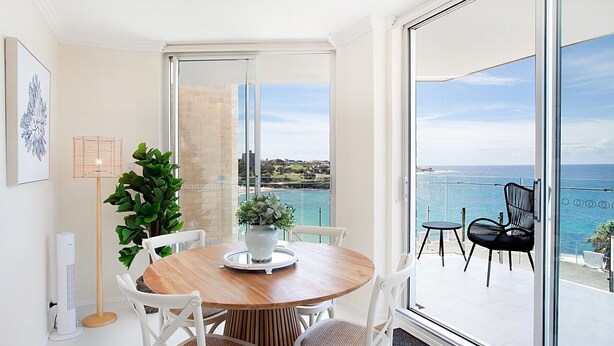 A dining area with a wooden table and white chairs, a potted plant, and a view of the ocean through large glass doors.
