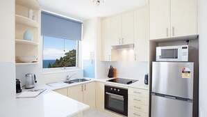 A modern kitchen with white cabinets, a built-in oven, a microwave, and a window with a view of the sea.