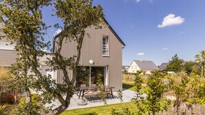 Ein modernes, zweistöckiges Haus mit einer Terrasse, die Gartenmöbel bietet.