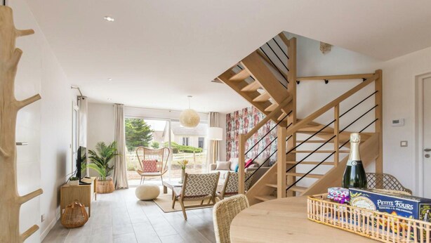 Ein modernes Interieur mit einer Holztreppe, einem runden Esstisch, Korbstühlen und Blick ins Freie.