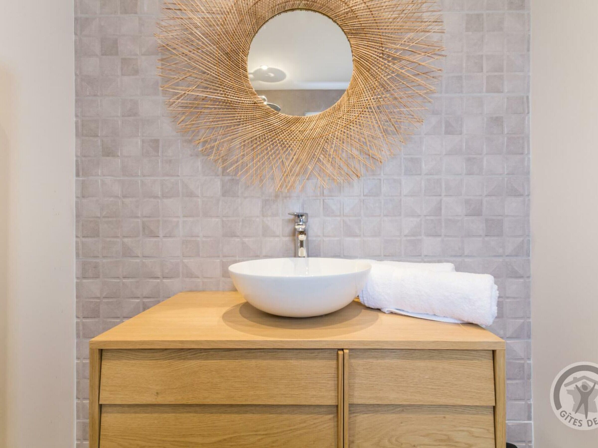 A bathroom with a round mirror, a white sink, and a wooden cabinet.