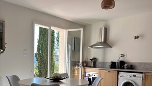 Une cuisine moderne équipée d’un lave-linge intégré, un coin repas avec une table ronde et des chaises, et une vue sur la verdure à l’extérieur.