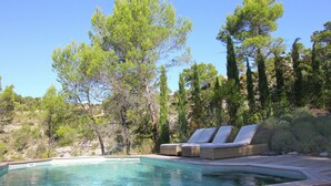 Un espace piscine doté de chaises longues et d’un jacuzzi, entouré d’arbres et d’un paysage vallonné.