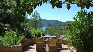Une terrasse extérieure aménagée avec des meubles en osier, offrant une vue sur un lac et des collines.