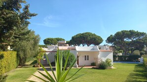 A white villa with a garden, a pathway, and a large tree in the foreground. - Casa Azevedo - Vilamoura (Vilamoura)