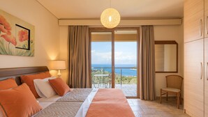 Una camera d'hotel con un grande letto, vista sul mare, un balcone e un'area pranzo.