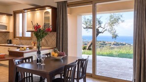 Una cucina moderna con zona pranzo, un'ampia finestra vista mare e un tavolo apparecchiato con frutta e bicchieri da vino.