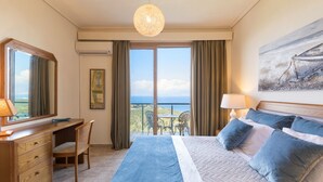 Una camera d'albergo con un letto grande, una scrivania, una sedia, un balcone con tavolo e sedie, e un quadro appeso al muro.