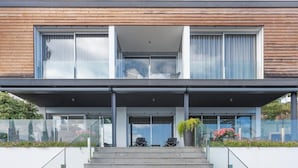 Une maison moderne à deux étages, dotée d’un porche avant couvert, de grandes fenêtres et d’un escalier menant à l’entrée.