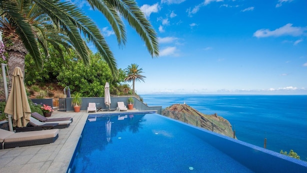 Une piscine à débordement offrant une vue sur l’océan, des chaises longues et des palmiers.