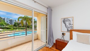Une chambre d’hôtel avec un balcon, donnant sur la piscine, comprenant un lit, une table de chevet et une œuvre d’art murale.