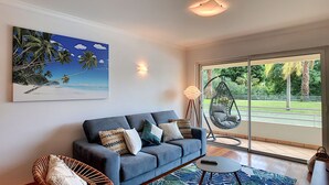 A living room with a sofa, cushions, a hanging chair, a lamp, and a large window with a view of greenery. - Aidan Apartment by LovelyStay (Funchal)
