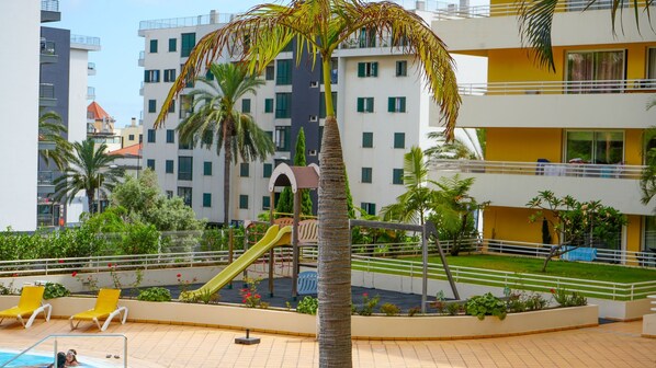 A pool area with a slide, palm trees, and a playground.