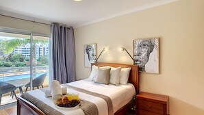 A hotel room with a bed, a bedside table, a tray with fruit, and artwork on the walls. - Aidan Apartment by LovelyStay (Funchal)