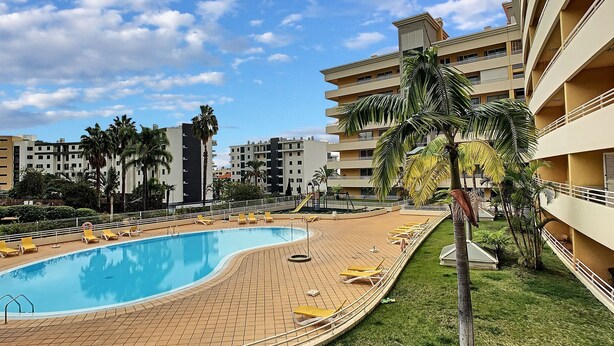 A swimming pool with lounge chairs, palm trees, and a multi-story building in the background. - Aidan Apartment by LovelyStay (Funchal)