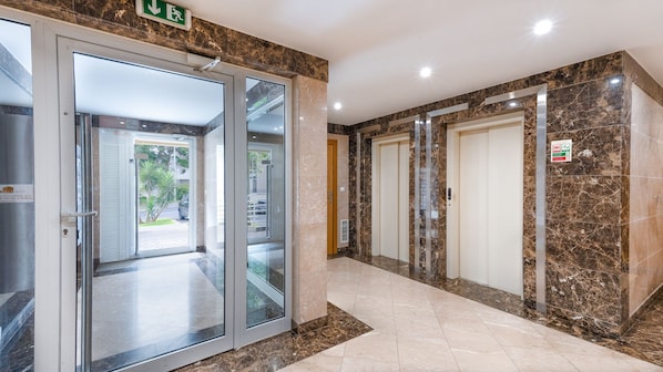 A hotel lobby with a glass door entrance, marble flooring, and two elevators. - Aidan Apartment by LovelyStay (Funchal)