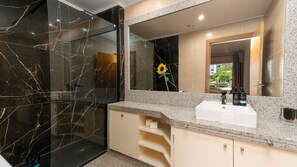 Une salle de bain moderne avec une douche à parois de verre, un grand miroir et un lavabo agrémenté d’articles de toilette.