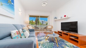 Un salon moderne avec un canapé, un téléviseur et un balcon offrant une vue sur les immeubles.