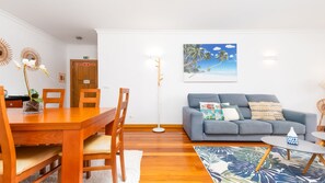 A room with a dining table, chairs, a grey sofa, a floor lamp, and a tropical-themed painting on the wall. - Aidan Apartment by LovelyStay (Funchal)