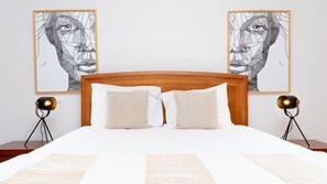 A bed with a wooden headboard, two pillows, and a white bedspread. There are two wall-mounted lamps on either side of the bed. - Aidan Apartment by LovelyStay (Funchal)
