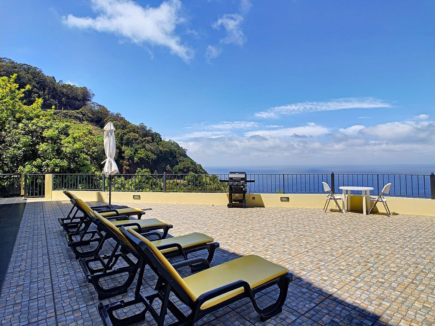 Une terrasse avec des chaises longues, un barbecue et une table avec des chaises, offrant une vue sur la côte.