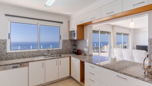 Een moderne keuken met granieten aanrechtbladen, witte kastjes en een groot raam met uitzicht op de zee.