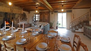 Een eetruimte met een houten tafel gedekt voor een maaltijd, een stenen openhaard en een trap naar een hoger gelegen verdieping.