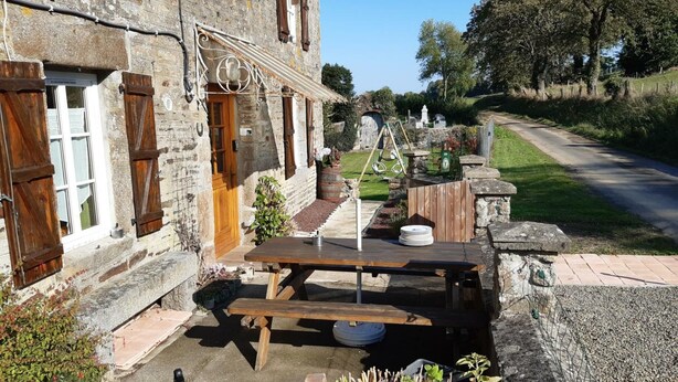 A stone building with a wooden door and windows, a picnic table, and a garden area with plants and a swing set.