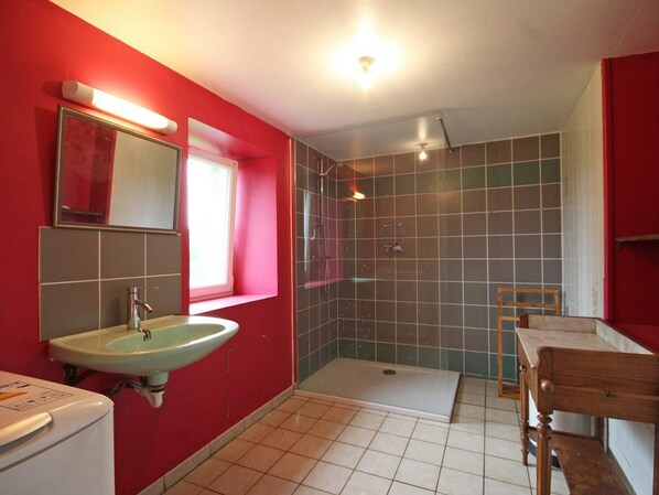 A bathroom with a sink, mirror, shower, and wooden bench.
