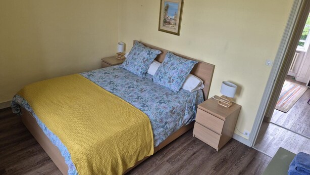 A bedroom with a bed, two bedside tables, a nightstand, a framed picture on the wall, and a door leading to an outdoor area.