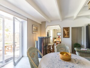A dining area with wicker chairs, a round table with a floral tablecloth, and a bowl of fruit. - Village house with private garden, perfect for families (Orval sur Sienne)