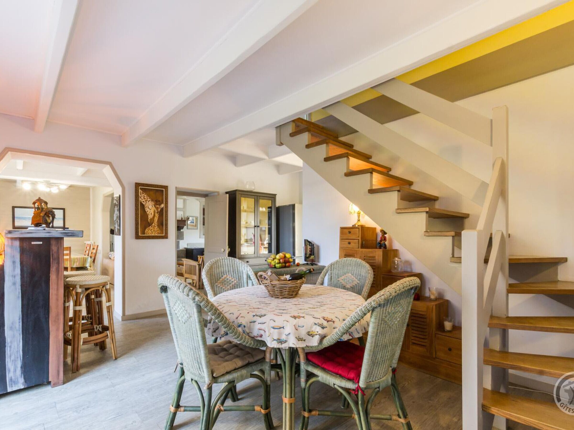 Ein Essbereich mit Korbstühlen und einem Tisch für vier Personen, eine Treppe mit Holzstufen und ein Schrank mit Glastüren im Hintergrund.
