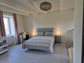 A bedroom with a bed, bedside lamps, a radiator, a window with curtains, and a hanging light fixture. - Village house with private garden, perfect for families (Orval sur Sienne)