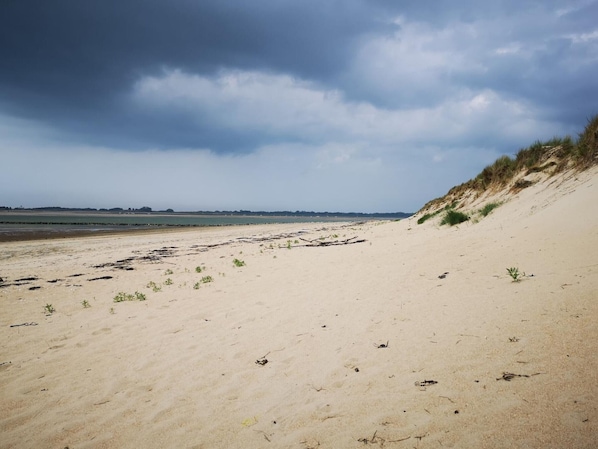 Une plage avec des dunes de sable et un ciel nuageux.