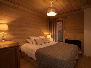 A wooden-paneled bedroom with a bed, a nightstand, and a hanging light fixture.
