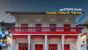 Un edificio de dos pisos con puertas rojas y columnas blancas, que incluye un balcón con barandillas rojas.