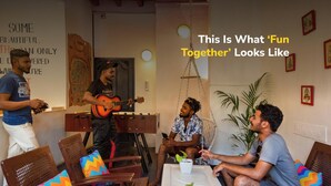Un grupo de personas en una habitación con un guitarrista, sillas con cojines de colores y una pared con citas motivacionales.