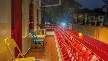 A balcony with a red railing, chairs, and a view of the street at night.